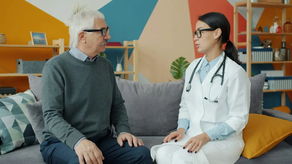 A clinician talks with an older man in his living room during a follow up visit