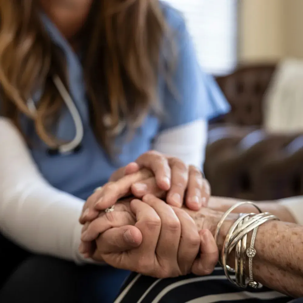 A caregiver gently holds the hands of an older woman