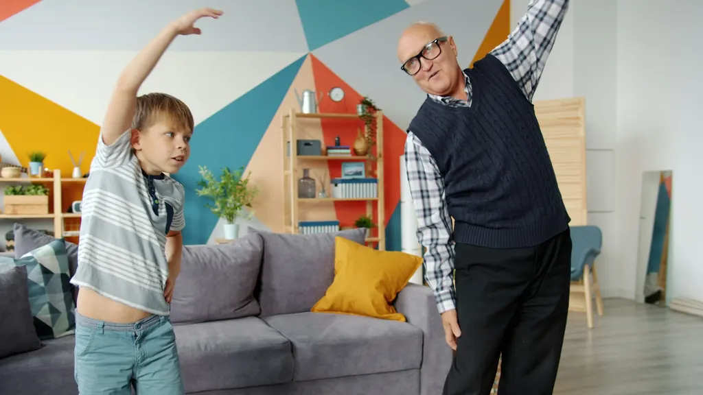 An older man and his grandson stretch together in a bright living room