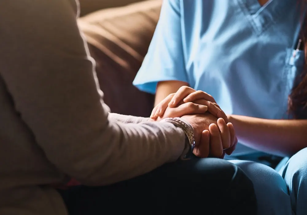 A nurse in navy scrubs holds the hands of an older patient