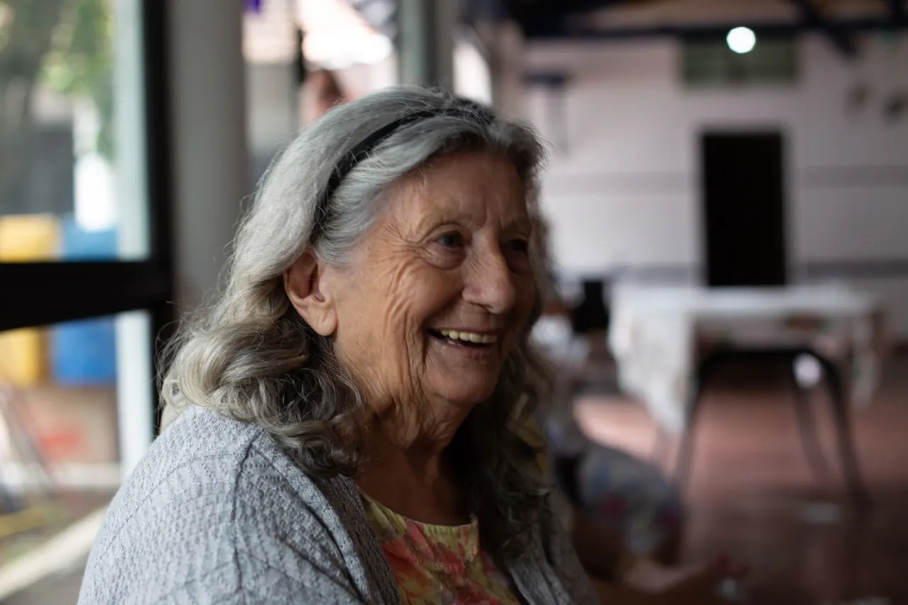 An older woman smiles warmly in a sunlit room
